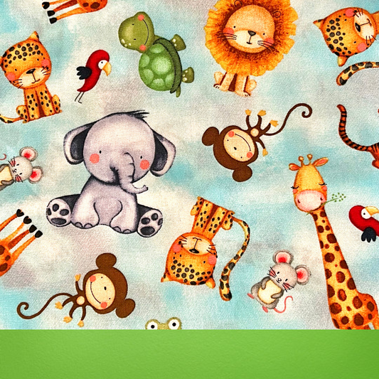 Close-up of Safari Sweeties Traditional Scrub Cap fabric showing blue background with white clouds and cute safari animals like lions and elephants with green trim
