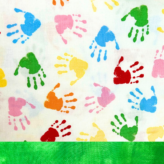 Close-up of Happy Hands Traditional Scrub Cap fabric featuring multicolor mini handprints on a white background with green trim