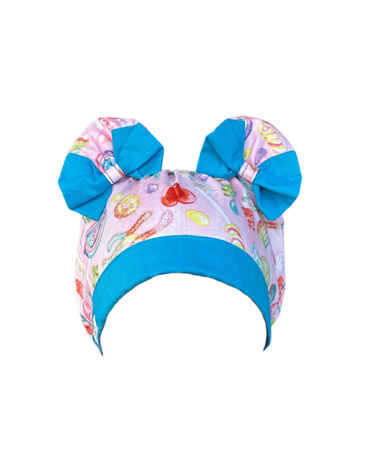 ScruBunz scrub cap with two space buns, pink background, colorful candy print, and sky blue accent trim
